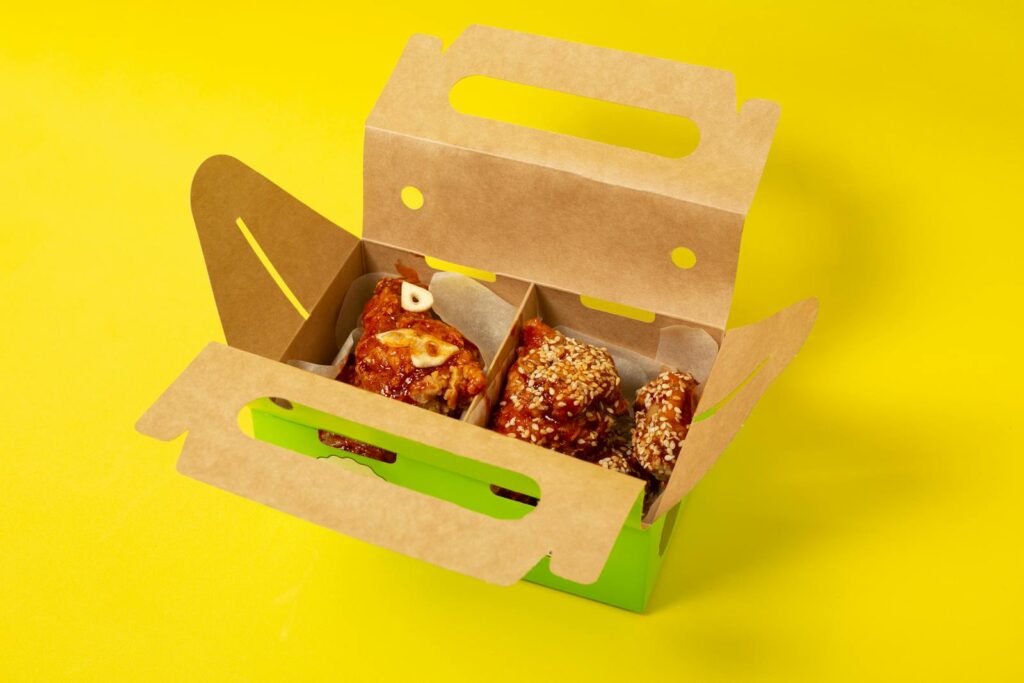 From above of appetizing chicken meat with garlic placed in cardboard box on yellow background in studio